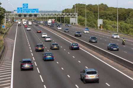 Mileage Tracking Traffordd aml-lôn brysur yn y DU gyda cheir a lorïau, arwyddion uwchben yn nodi llwybrau'r M1, yr M25, a'r A405